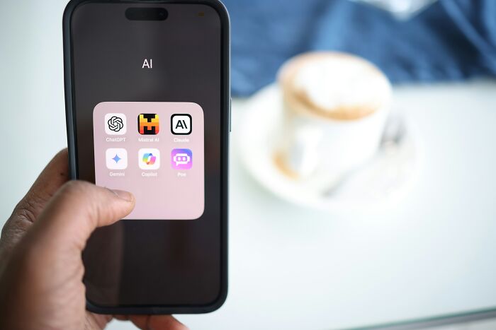 Hand holding a smartphone displaying various AI apps, including ChatGPT, Mistral AI, Claude, and Gemini.