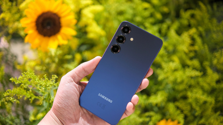 a hand holding a Samsung Galaxy phone near sunflowers