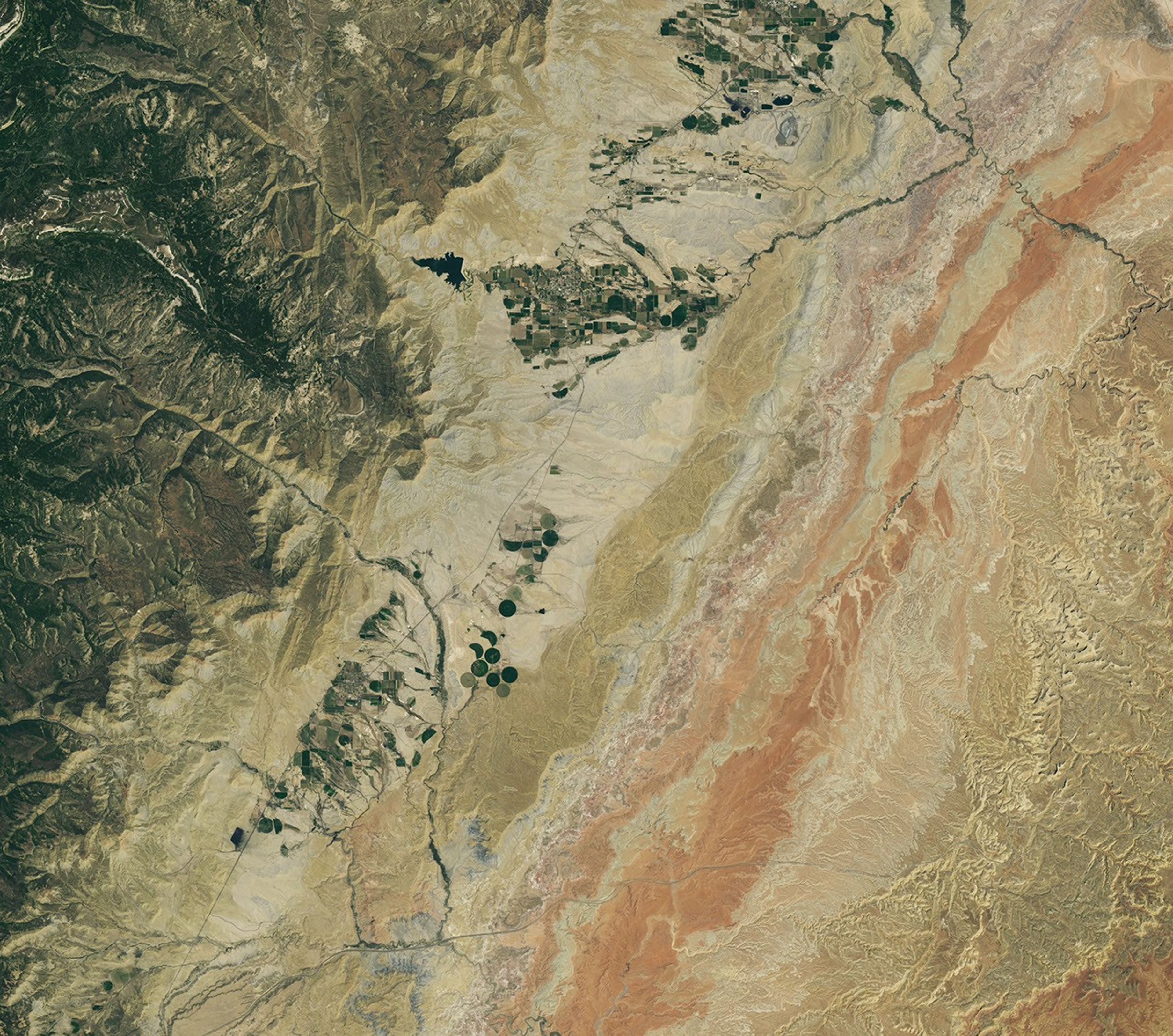 A dry, tan-colored valley containing a few circular irrigated fields runs roughly north-south through the image.