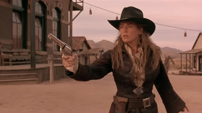 Sharon Stone's Ellen "The Lady" McKenzie stands holding her pistol in a frontier town street in The Quick and the Dead