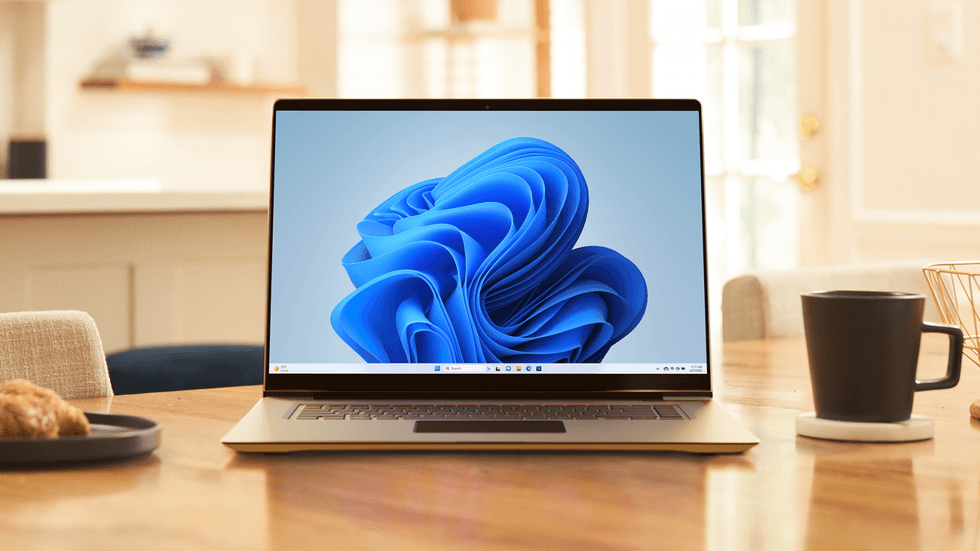 windows 11 laptop pictured on a wooden table with a cup of coffee beside it