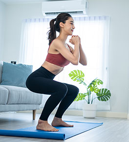 A dark-haired young woman with a ponytail does squatting exercises on a blue mat.