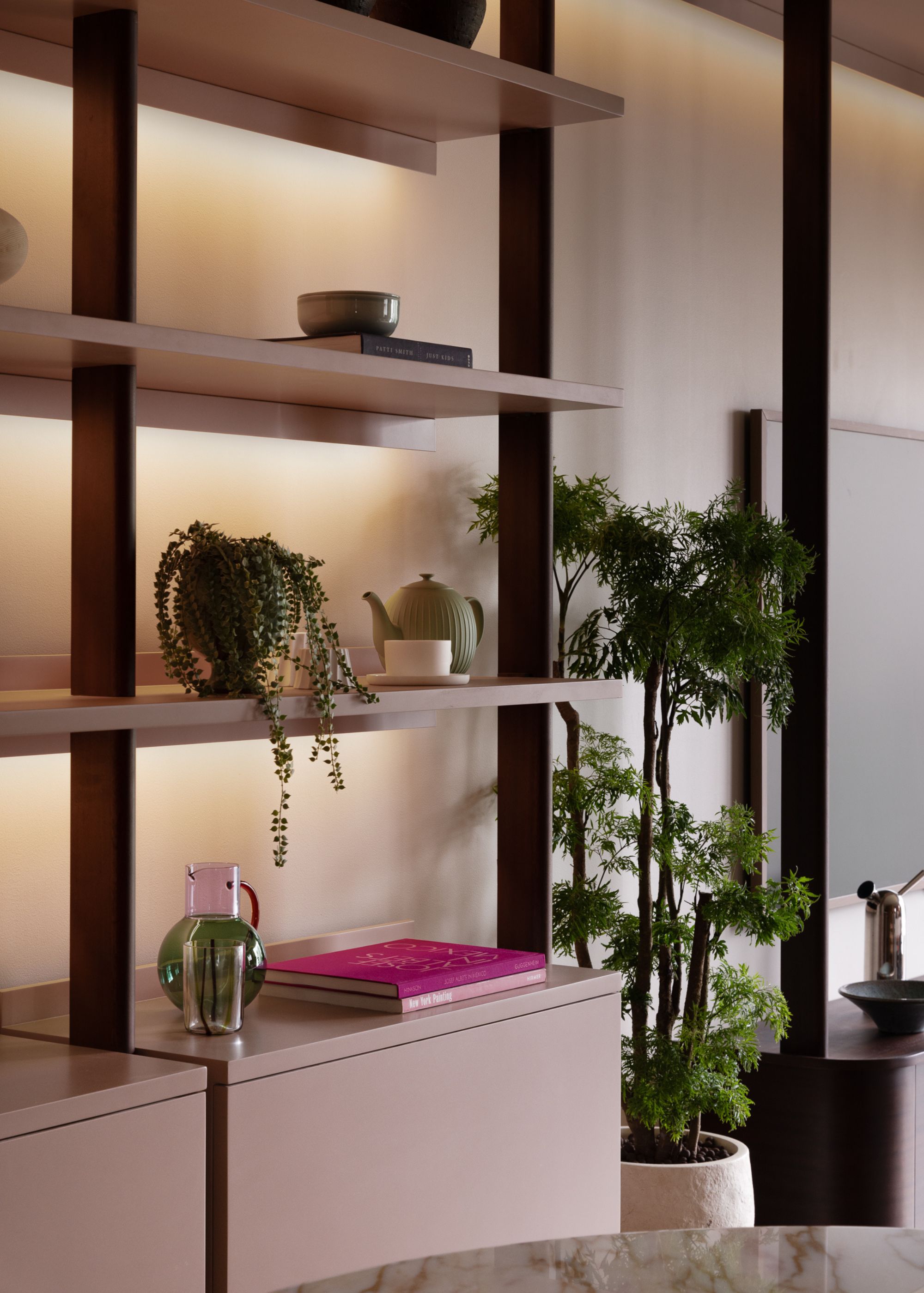 A living room with a shelf with backlighting styled with potted plants, coffee table books and ceramics