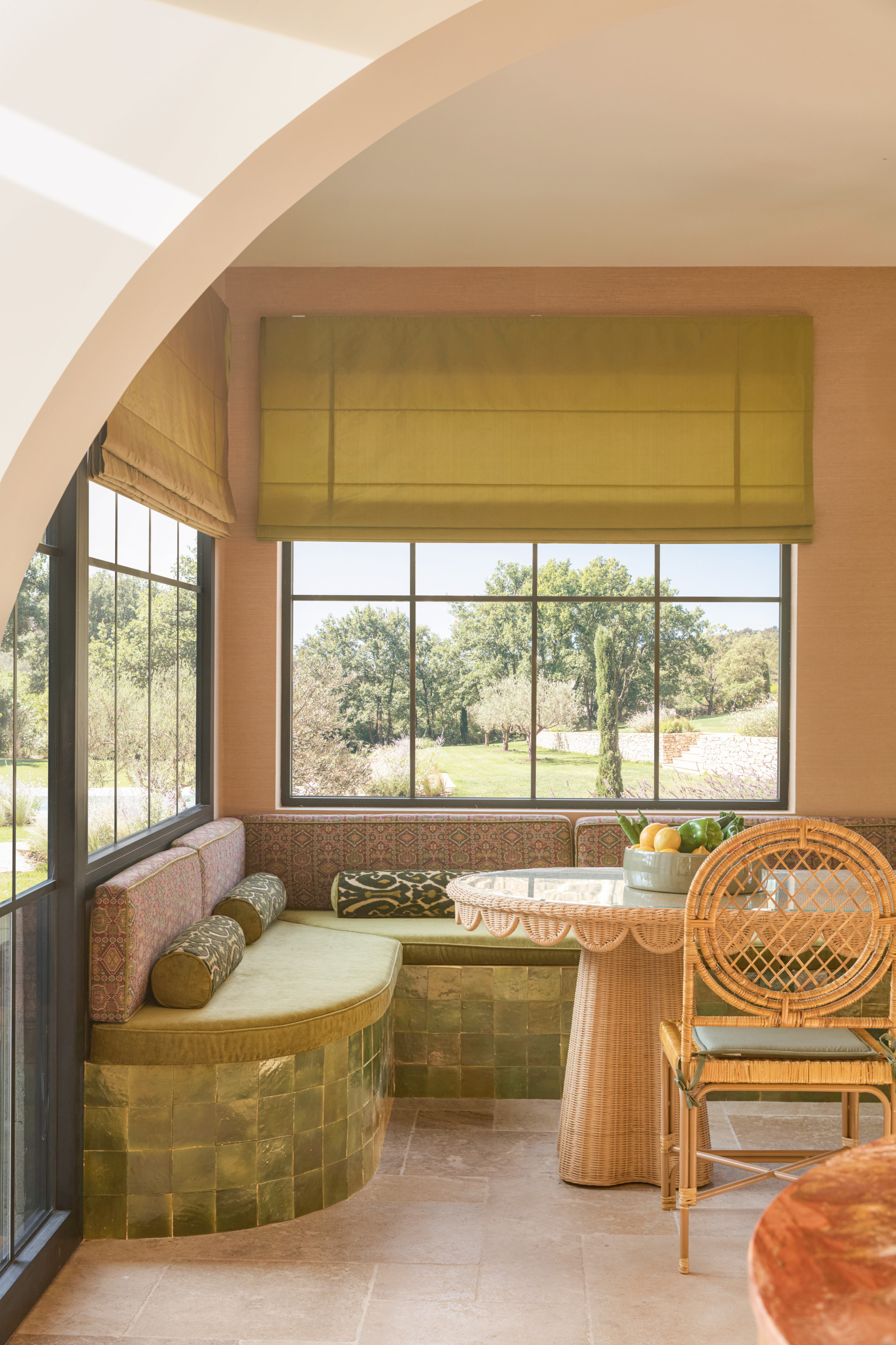 Breakfast nook with green tiled banquette seating, rattan dining table, cane chairs and green blinds