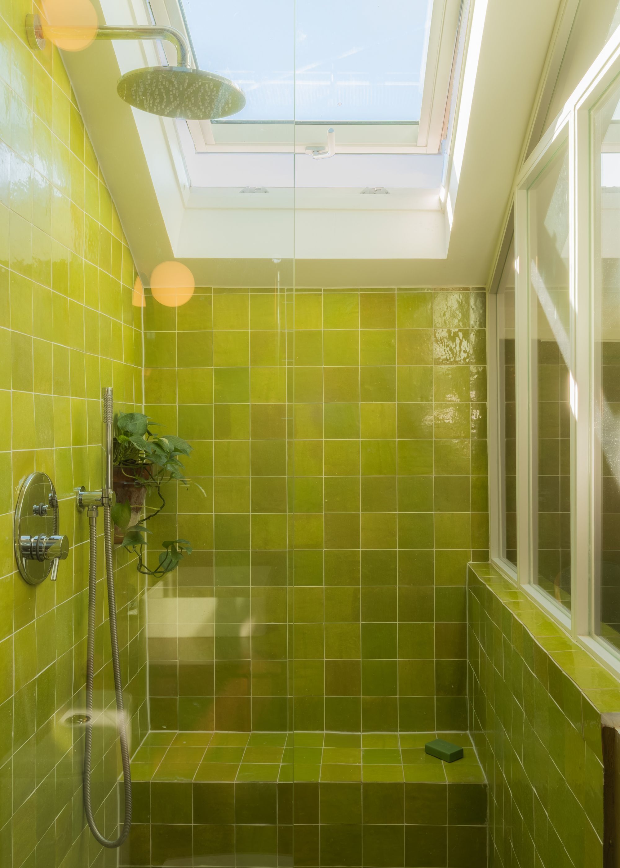 A bathroom fully tiled green with large window openings on top