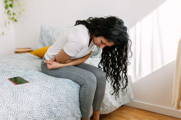 Young millennial woman suffering with stomach pain, feeling unwell sitting on bed in the morning Young millennial woman suffering with stomach pain, feeling unwell sitting on bed in the morning