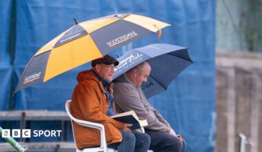 Two spectators hold up umbrellas in the rain at Forfarshire Cricket Club