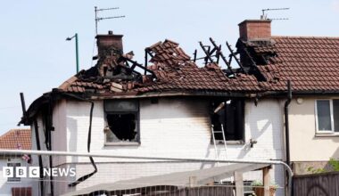 The roof of the property is badly burnt. There are pieces of wood or metal sticking up out of it. The holes where the windows were are blackened.