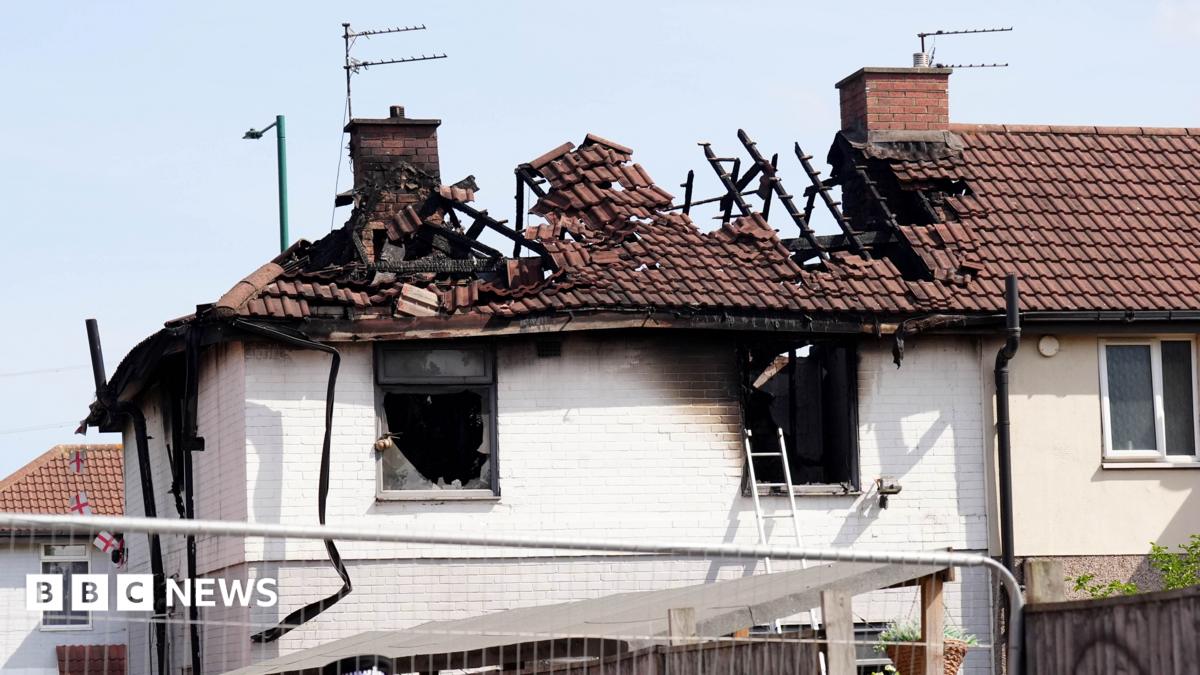 The roof of the property is badly burnt. There are pieces of wood or metal sticking up out of it. The holes where the windows were are blackened.
