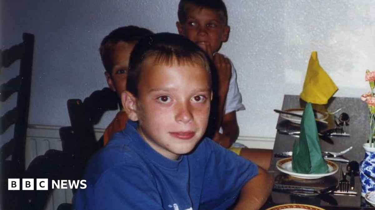 Anton wearing a blue t shirt on the left. There are several other people smiling at the camera as they sit down at a dinner table. There are green and yellow napkins on plates.