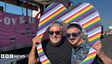Two men stand within a cut-out rainbow heart