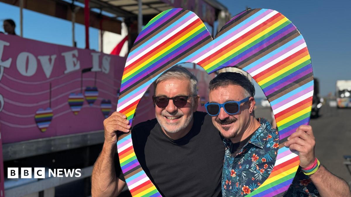 Two men stand within a cut-out rainbow heart