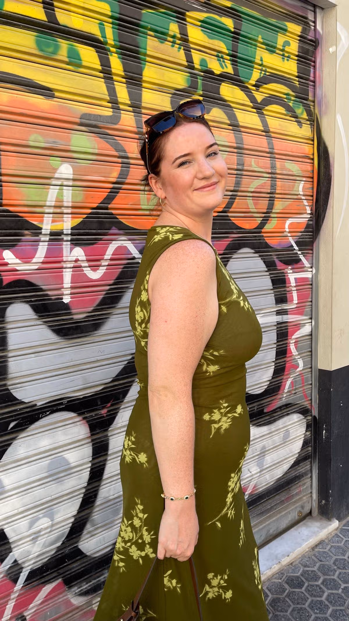 A young woman in a green dress against a backdrop of graffiti on a wall