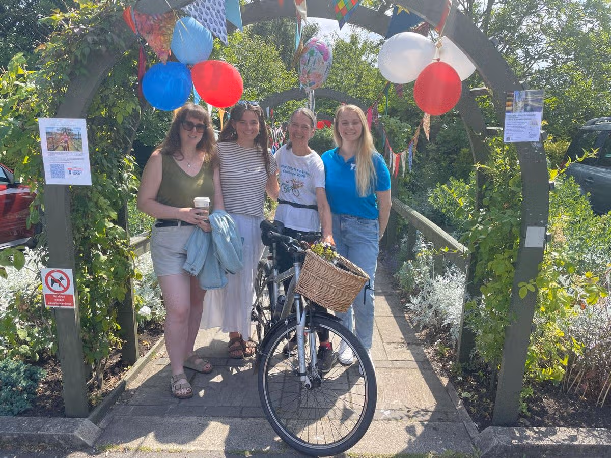 An image of four women standing under a wooden arch covered in flowers, vines and balloons.