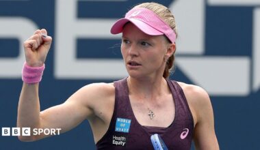 Harriet Dart, wearing a purple dress and pink visor, holds her racquet in her left hand and raises a clenched right fist