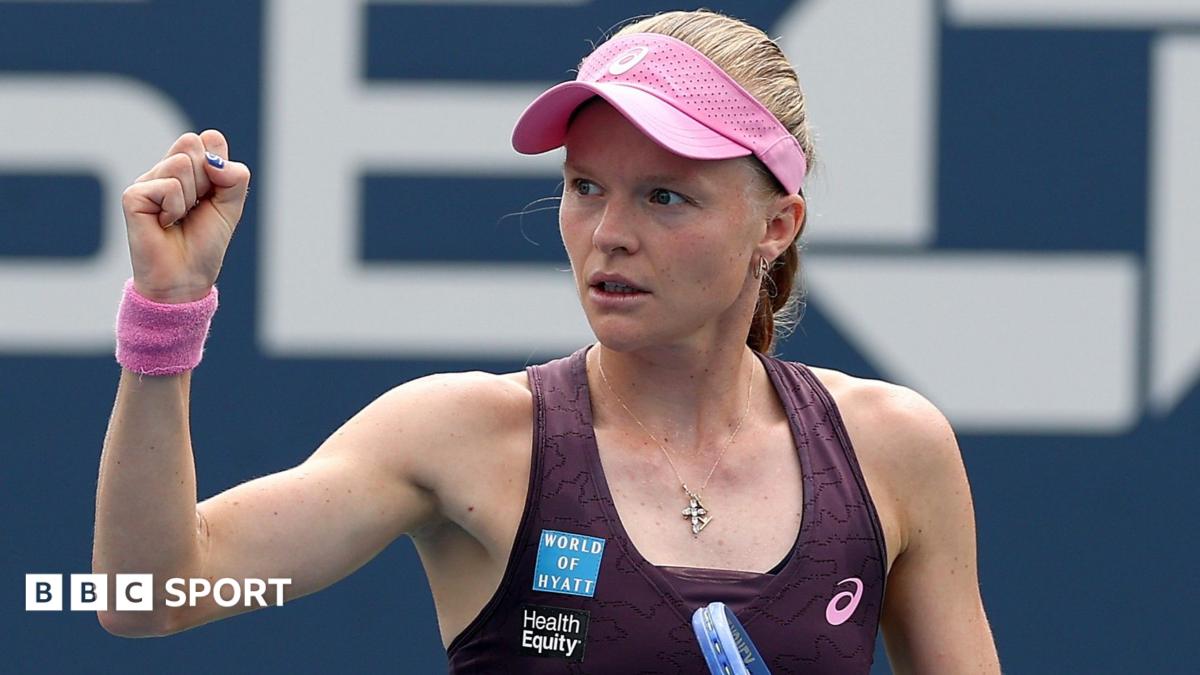 Harriet Dart, wearing a purple dress and pink visor, holds her racquet in her left hand and raises a clenched right fist