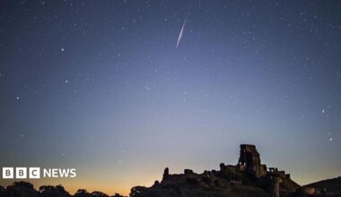 A bright Perseid meteor streaks across a star-filled night sky above the silhouette of Corfe Castle