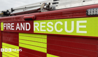 The side of a fire engine with red and green/yellow rectangles in a pattern and "fire and rescue" written on the side.