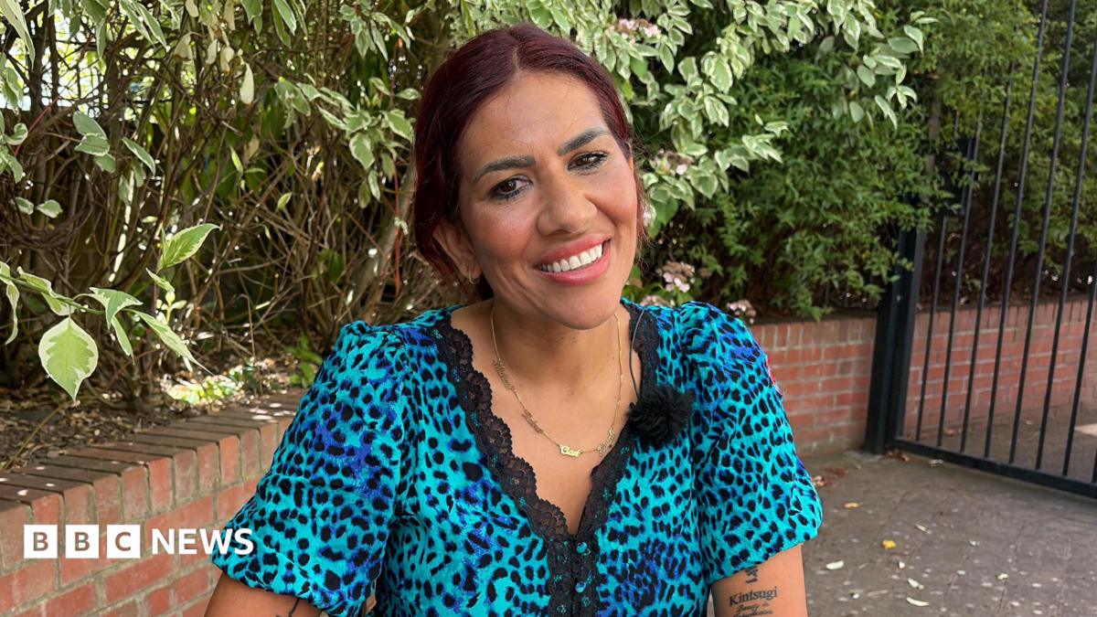 A woman with dark hair and a blue animal print dress smiles sitting in a garden.