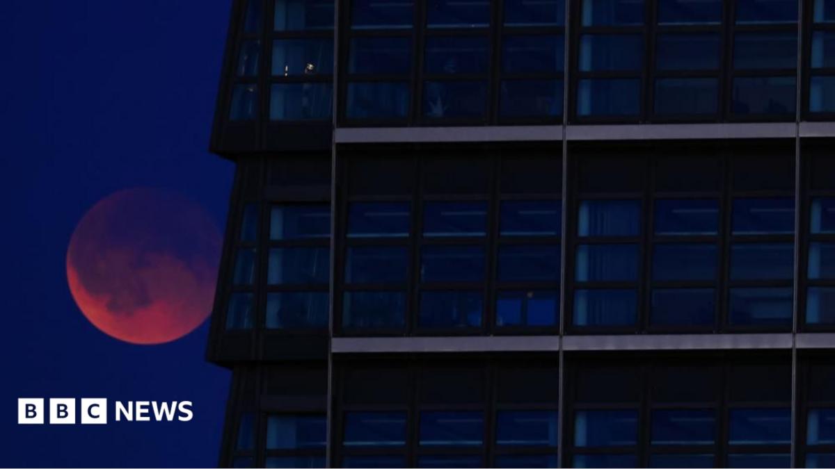 A red Moon lurking behind a glass skyscraper.