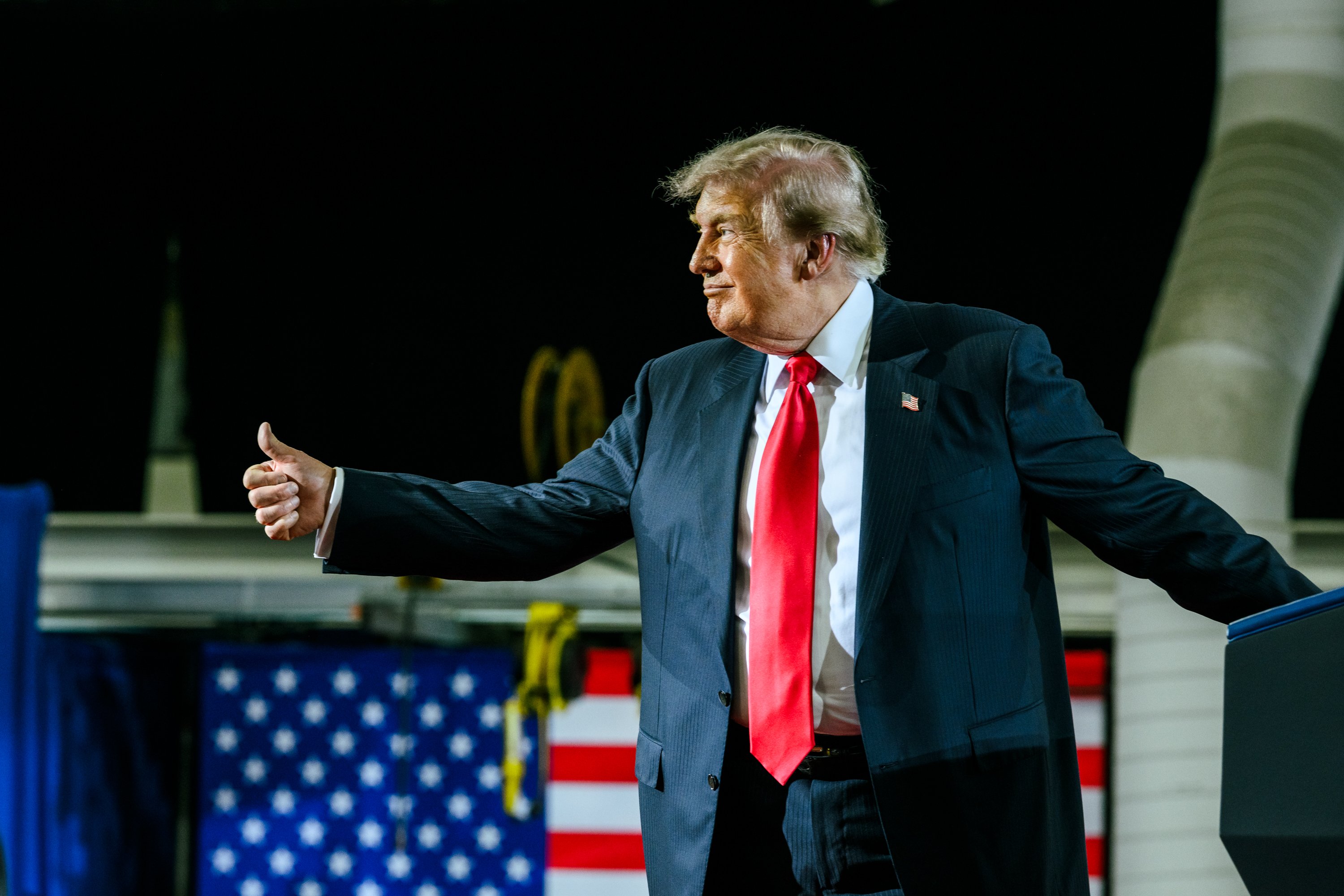 Donald Trump giving a thumbs-up to a crowd during a speech. 