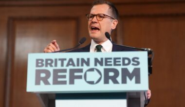 Robert Jenrick speaking at a podium with BRITAIN NEEDS REFORM sign, delivering a speech.