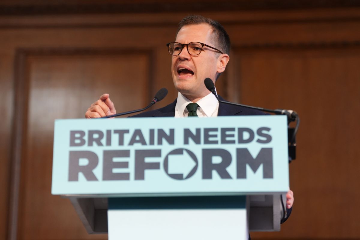 Robert Jenrick speaking at a podium with BRITAIN NEEDS REFORM sign, delivering a speech.