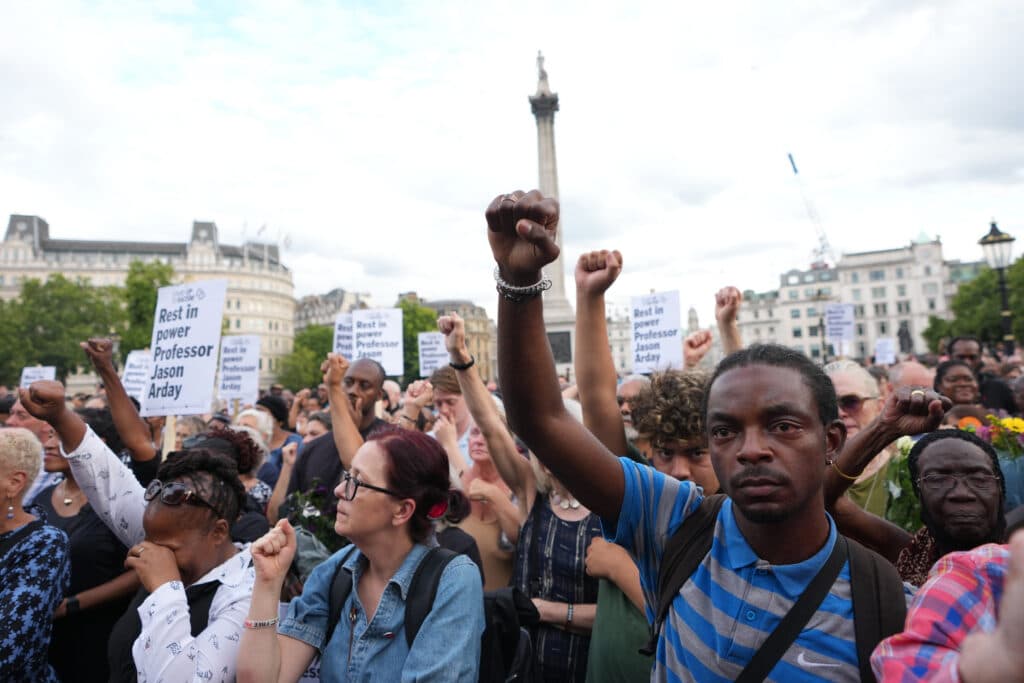 Crowd at Trafalgar Square raising fists, holding signs reading "Rest in power Professor Jason Arday