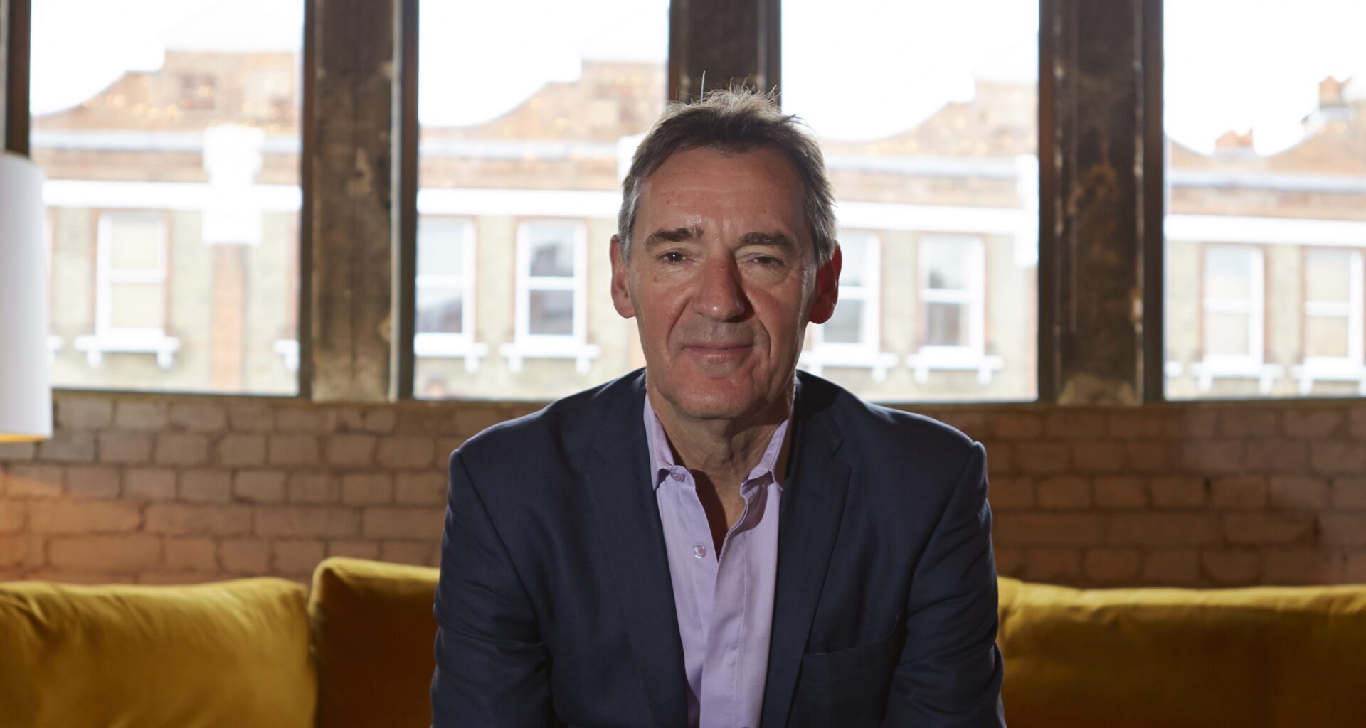 Jim ONeill, economist and former Goldman Sachs chairman, sitting on a yellow sofa in front of large windows.