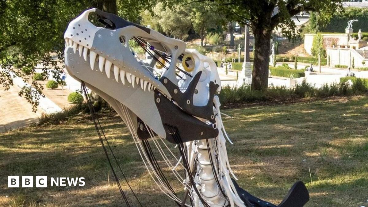 A white and black foam sculpture of Megalosaurus resting on its belly on the grass.