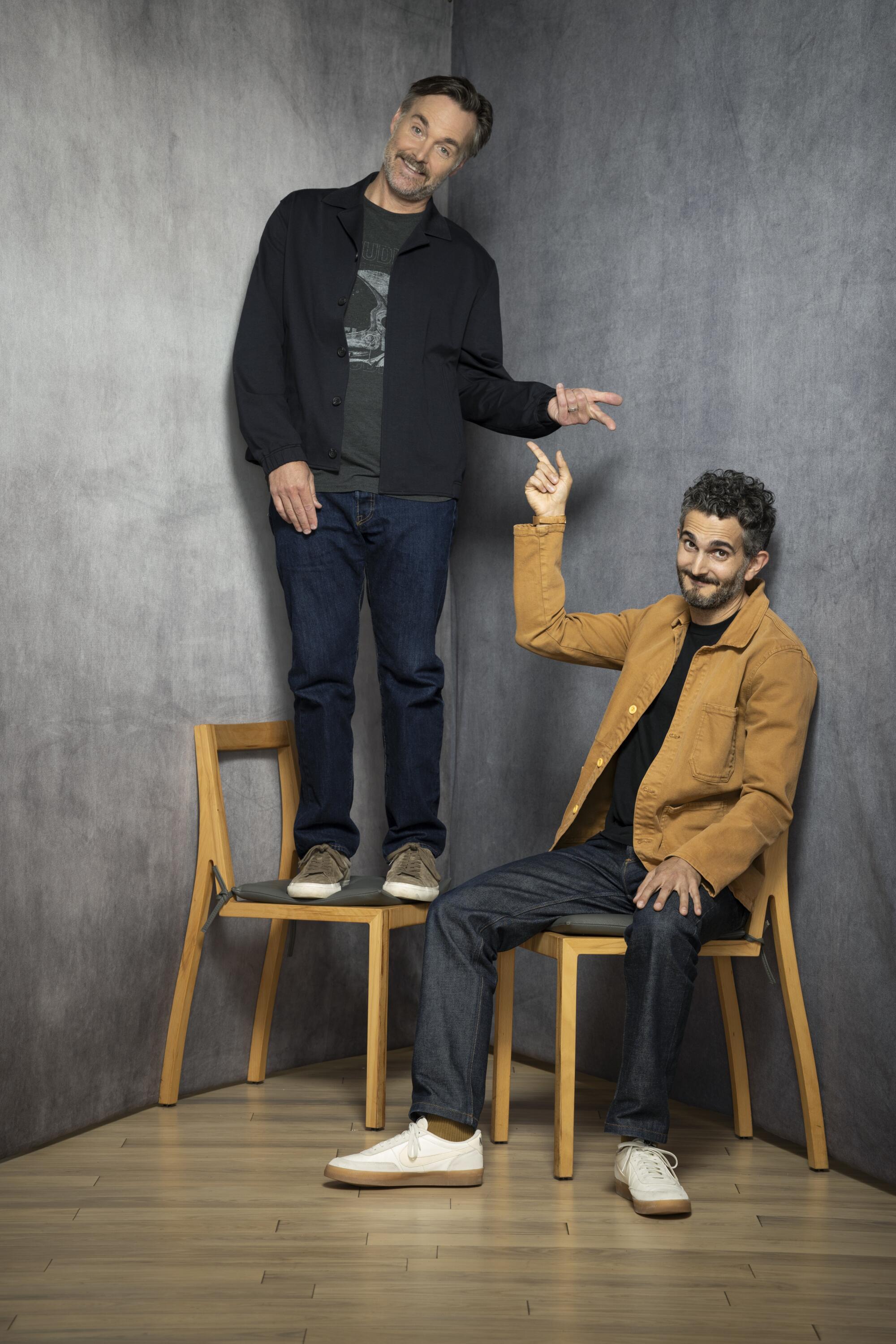 A man stands on a chair next to a seated man who points up.