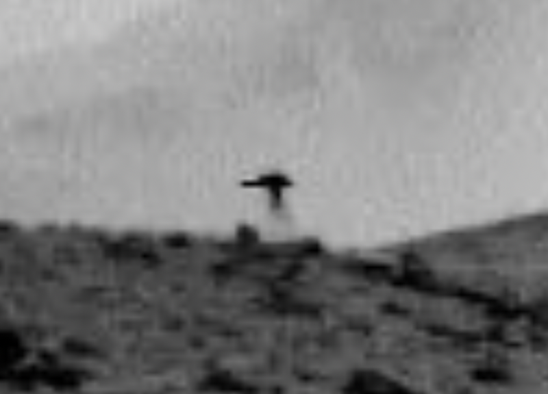 Jellyfish on Mars: Fuzzy, black and white view of a rocky hill, with a dark jellyfish-like shape on top of it.