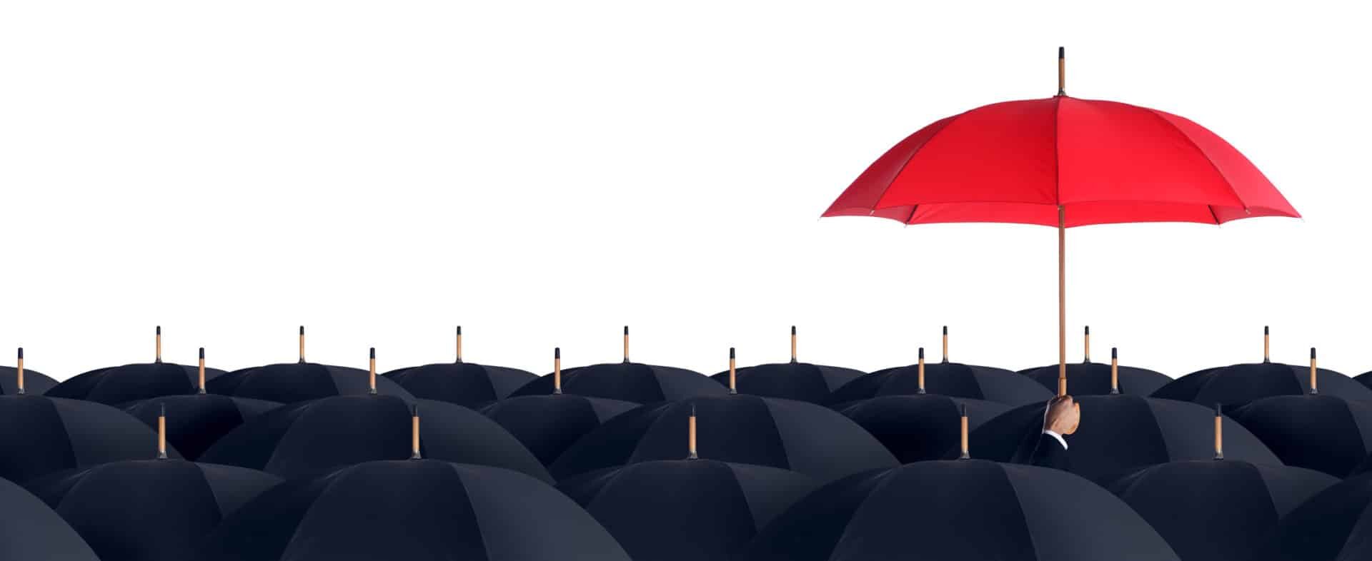 A red umbrella stands higher than a crowd of black umbrellas.