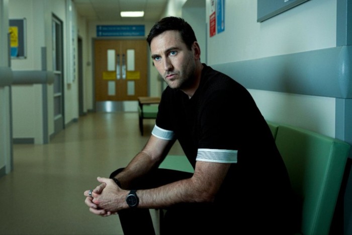 coronation-street-male-breast-cancer-storyline Jacob Roberts as Kit Green in Coronation Street sat on a waiting room chair in a hospital leaning and supporting his weight on his knees.