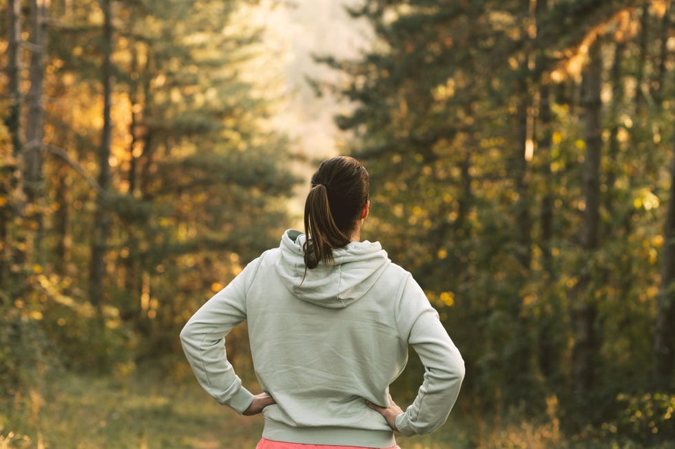 treadmill vs outdoor walking: the back of a woman as she looks into the trees, with hands on hips