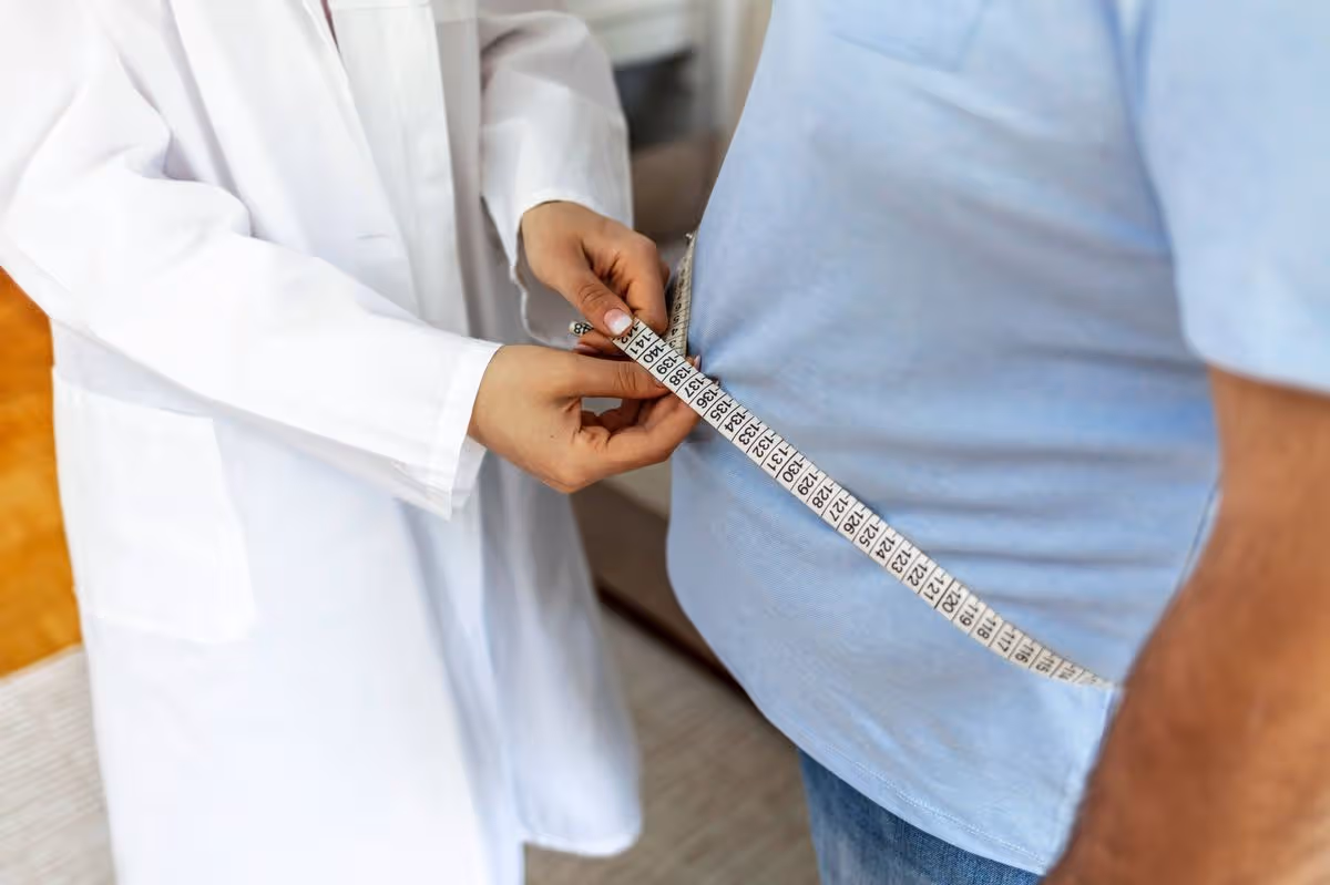 Women doctor measuring overweight man in clinic. Young female doctor measuring fat layer of overweight man with tailor tape in clinic. Eating, diet and unhealthy life concept. Copy space.