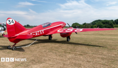 Red plane on a grass airfield. It has the number 34 painted on the tail fin.