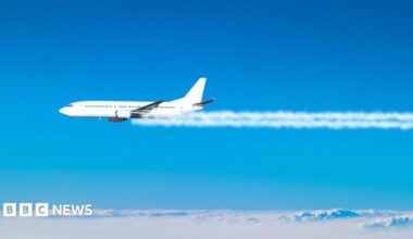 A jet plane flies across the blue sky, with white contrails coming from its engines