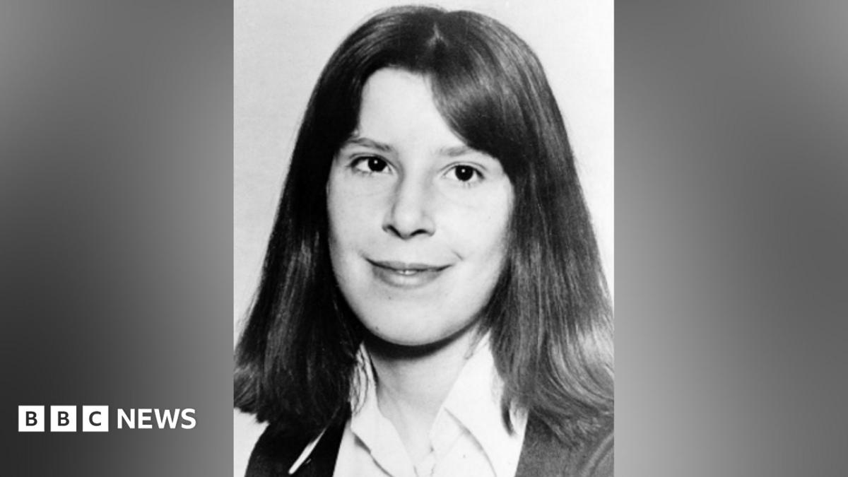 A black and white image of Suzanne Lawrence, who has shoulder-length hair and wears a shirt and cardigan.