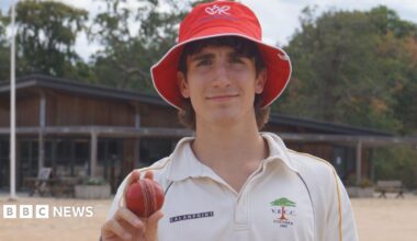 A man dressed in cricket whites holding a cricket ball.