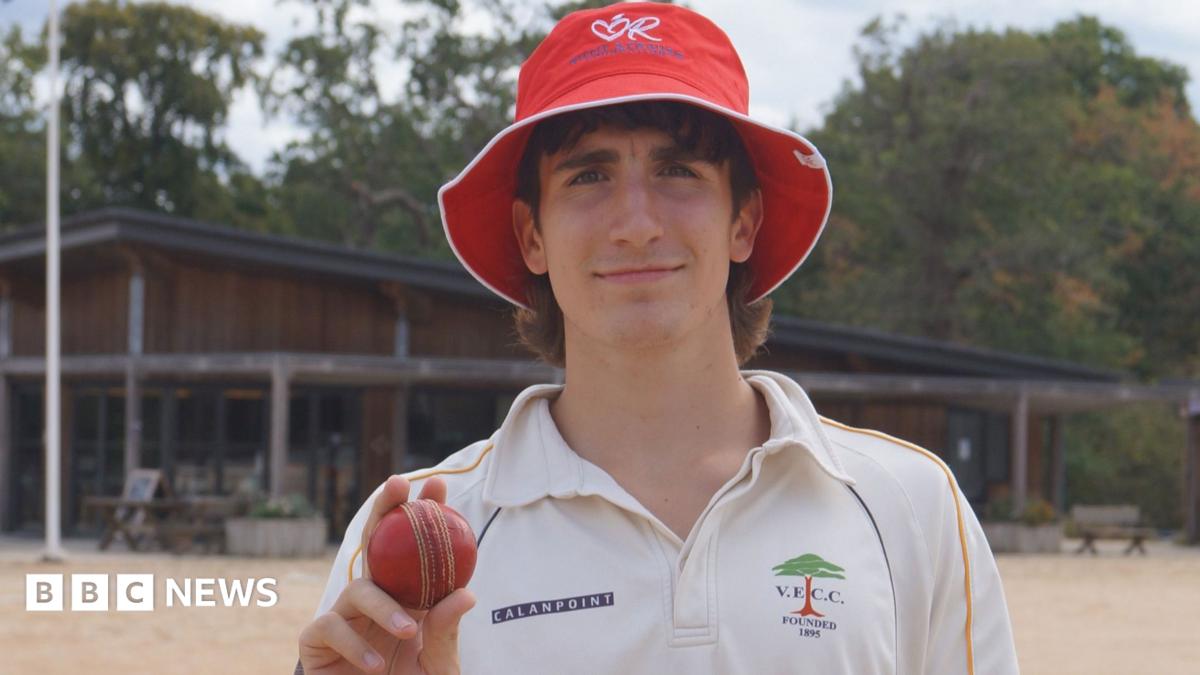 A man dressed in cricket whites holding a cricket ball.