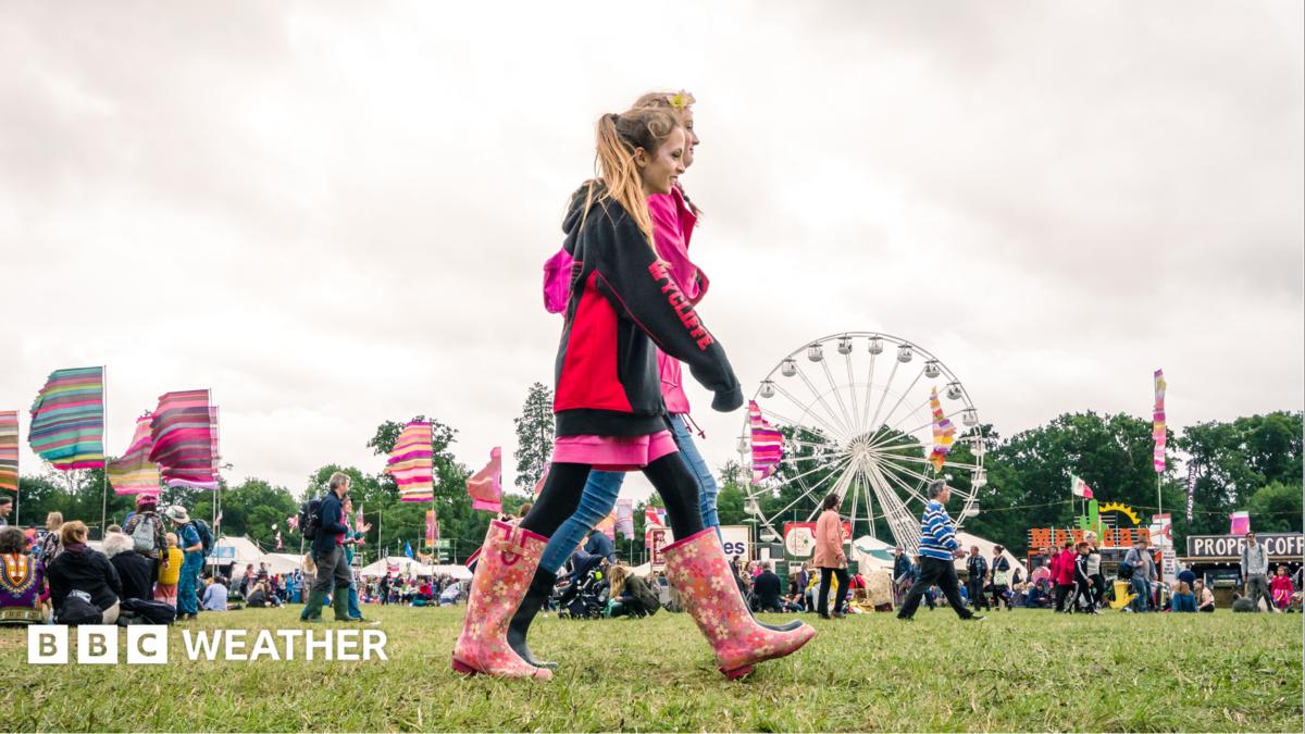 Two people walk through a festival site wearing waterproofs and wellies