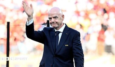 Gianni Infantino waves while wearing a dark blue suit with a Fifa pin