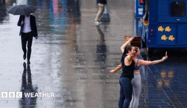 wet street with a man walking along with an umbrella and two women posing for selfie in the rain