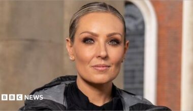 Carlos Gu and Amy Dowden pictured side by side in a promotional photo for the Channel 4 show, Celebrity Hunted. Carlos is wearing a grey dark coat, a light grey t-shirt and several necklaces. Amy is wearing a black top, jacket and coat. They are both looking at the camera and are not smiling.