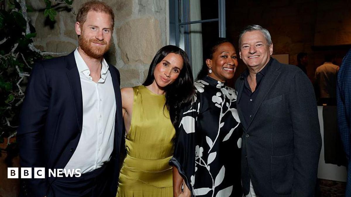 Harry and Meghan smiling next to two others, wearing cocktail attire, at a house