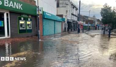 A street with shops along the left and flood water pooling outside.