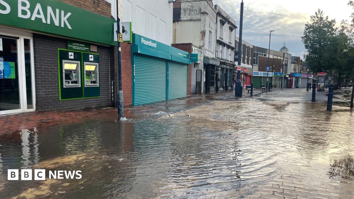 A street with shops along the left and flood water pooling outside.