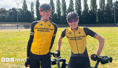 Three men and Parker in cycling helmets are standing up holding a bike each. They are looking at the camera and in a line along with Porter and Lonsbrough, who are in the middle. Parker is second from the left.