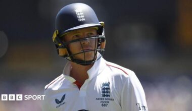 Ollie Pope, wearing a blue helmet and white England shirt, looks to his left